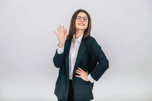 Joven empresaria confiada en traje negro de pie, levantando la mano, sonriendo ampliamente, otra mano akimbo . — Foto de Stock