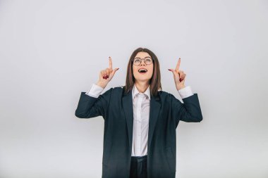 Siyah takım elbiseli güzel bir iş kadını ayakta, gülümsüyor, yukarı bakıyor, metin ya da ürün için parmaklarını havaya kaldırıyor..