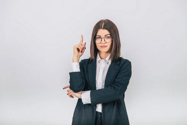 Pretty young businesswoman in black suit standing, looking at the camera, pointing her finger up at the copyspace for text or product. — Stock Photo, Image