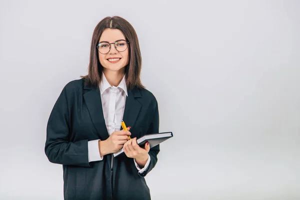 Young businesswoman in black suit holding a notebook and yellow pen, looking at the camera, smiling. — Stock Photo, Image