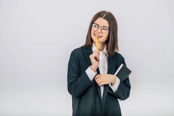 Pretty young businesswoman in black suit standing, notebook and pen in her hands, thinking what to write. — Stock Photo, Image