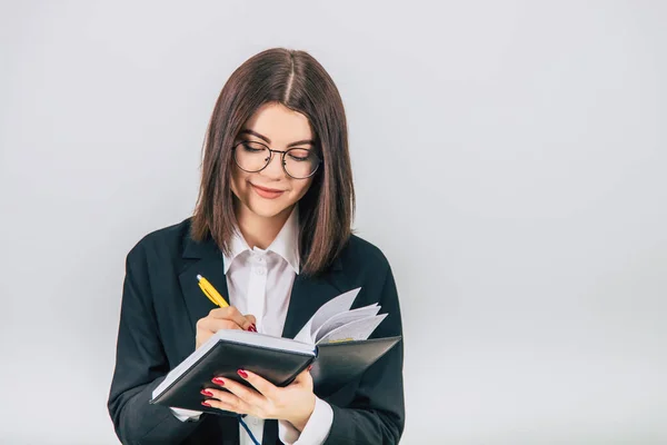 Pretty young businesslady in black suit standing, listening attentively, noting something in her notebook. — Stock Photo, Image