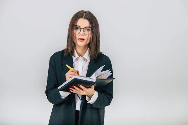 Pretty young businesslady in black suit standing, listening attentively, noting something in her notebook. Inquisitive face expression. — Stock Photo, Image