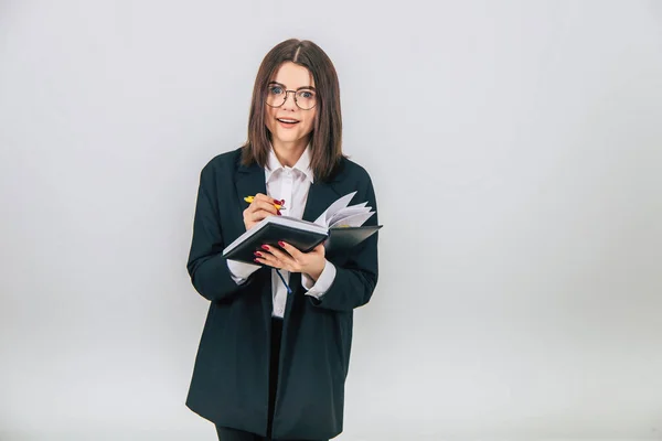 Pretty young businesslady in black suit standing, listening attentively, noting something in her notebook. Inquisitive face expression. — Stock Photo, Image