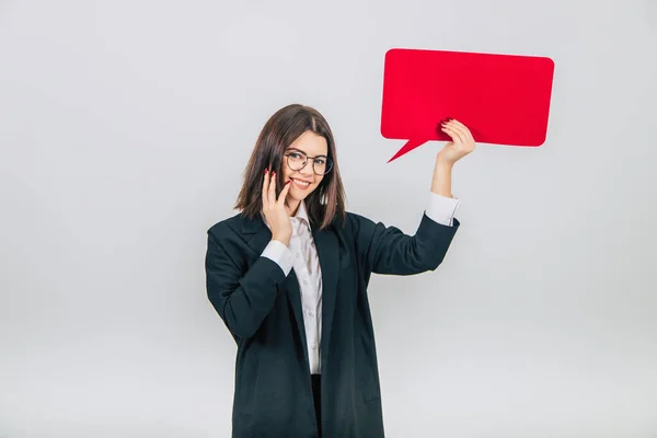Portrait of an excited young business woman raising up empty square red speech bubble, looking at the camera, smiling lovely, keeping hand on her cheek. — Stock Photo, Image