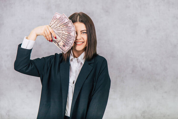Confident young businesswoman hiding her eye behind a fan of money banknotes.