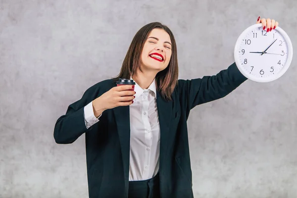 Bonita empleada levantando el reloj blanco, sonriendo, felizmente, sosteniendo una taza de café, mostrando que es hora de tomar un café al fin . —  Fotos de Stock