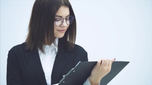 Geïnspireerd zakenvrouw in zwart pak staat met klembord in haar handen, draait het naar de camera, glimlachend. Het woord "zaken" staat op het blad papier.. — Stockvideo