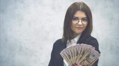 Kendine güvenen genç iş kadını kameraya dolar banknotları uzatıyor, poz veriyor, baştan çıkarıcı ve hoş bir şekilde gülümsüyor. Önde bulanık dolar var..
