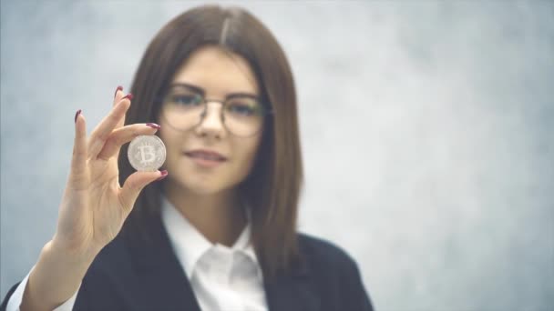 Suddigt leende ung affärskvinna i formell svart kostym visar ett silvermynt. Fokusera på myntet i framkant. — Stockvideo