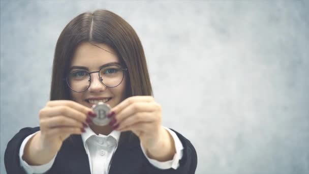 Selbstbewusste junge Geschäftsfrau im formalen schwarzen Anzug, die lächelnd eine Silbermünze in die Kamera reckt. Die Münze ist im Vordergrund verschwommen. — Stockvideo