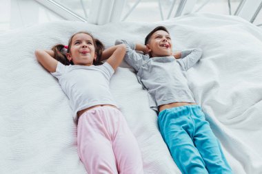 İki tatlı çocuk kanepede uzanıyor, elleri başının üstünde, dilleri dışarıda, uyumaya hazır..