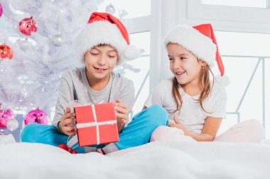 Noel Baba şapkası ve pijama giyen ve Noel hediyesi kutularını paylaşan iki çocuk..