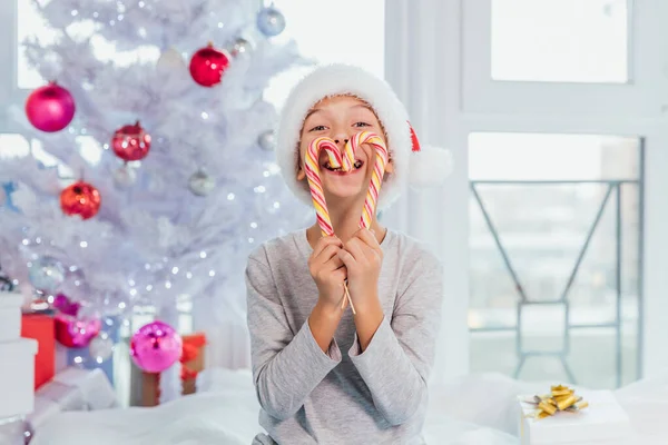 Mały cukiereczek trzyma pyszne cukierki przed ustami, patrzy prosto w kamerę, śmiejąc się, odizolowany ponad białym tłem nowego roku. — Zdjęcie stockowe