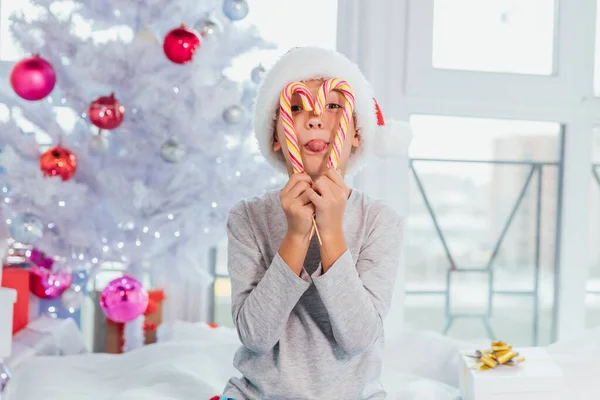 Tomten tittar genom ett godis sockerrör hjärta, lägga ut tungan, nära julgranen. — Stockfoto
