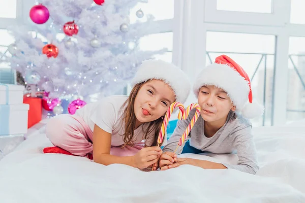 Чарівні кавказькі діти насолоджуються Різдвяним ранком, граючи в ліжку, роблячи серце з цукеркових паличок . — стокове фото