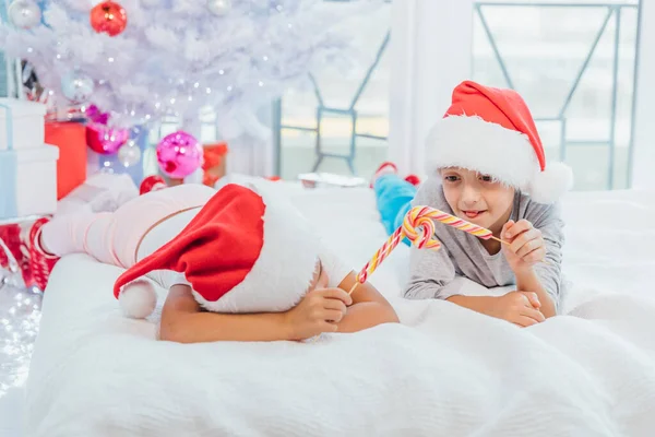 Ambiance chaleureuse de Noël dans laquelle sœur et frère joyeux jouant avec des cannes à bonbons, imitant une bagarre à l'épée . — Photo