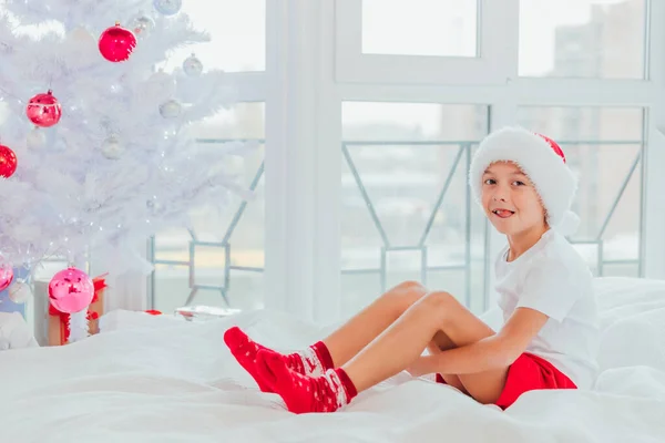 Menino bonito vestido como mini Santa ou elfo está sentado perto da árvore de Natal com um monte de presentes . — Fotografia de Stock