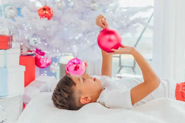 성탄절 트리 아래누워 있는 어린 아이의 모습, 공을 만지는 모습, 장식품 유리에 비친 자신의 모습. — 스톡 사진