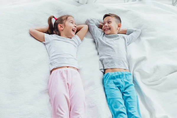 Vista superior de dos hermosos hermanos acostados en una cama juntos, sonriendo mientras descansan . — Foto de Stock