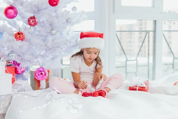 Jolie petite fille joue avec des flocons de neige décor près de l'arbre du Nouvel An, souriant belle . — Photo