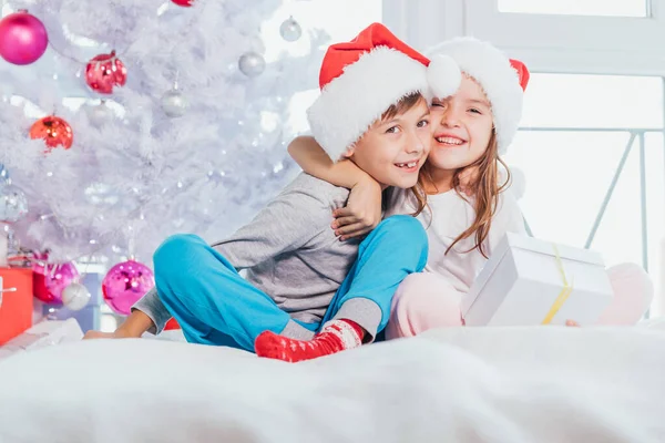 Dos jóvenes felices niños riendo lindo, niño y niña, hermano y hermana divirtiéndose en la mañana cerca del árbol de Navidad . — Foto de Stock