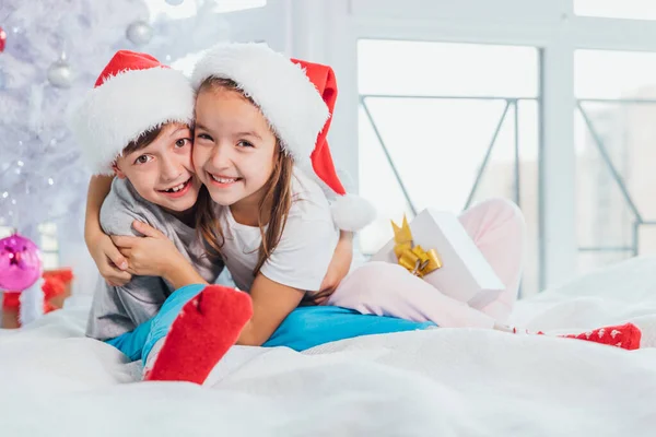 Dos jóvenes felices niños riendo lindo, niño y niña, hermano y hermana divirtiéndose en la mañana cerca del árbol de Navidad . — Foto de Stock