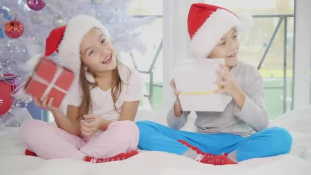 Full-body video of cute children sitting in lotos position with Christmas presents, shaking, knocking, listening to what is inside. — Stock Video