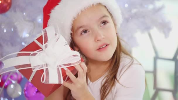 Vidéo recadrée d'une fille curieuse avec des cadeaux de Noël, tremblant, frappant, écoutant, essayant de savoir ce qu'il y a à l'intérieur . — Video