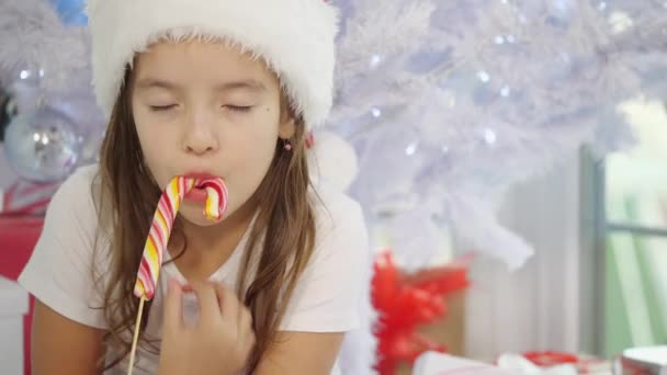 La niña bonita está probando una caña de azúcar, en la mañana de Navidad, mirando curioso . — Vídeo de stock
