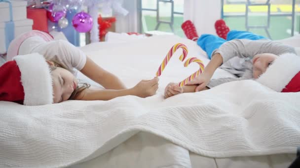 Adorables niños caucásicos disfrutan de la mañana de Navidad, jugando en la cama, haciendo corazón de bastones de caramelo . — Vídeo de stock