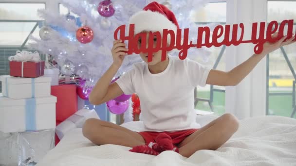 Funny funky boy is raising up red Happy New Year text, making fun, putting his tongue in hole of one of the letters. — Stock video