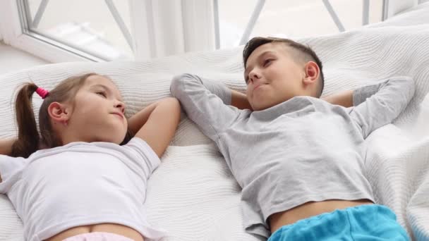 Yatakta birlikte uzanan, gülümseyen ve dinlenirken konuşan iki güzel kardeşin manzarası.. — Stok video