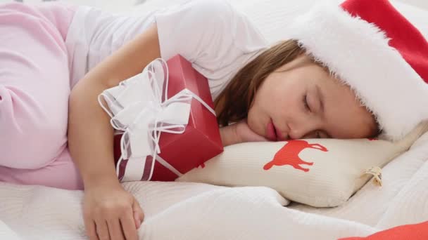 可爱的视频，小女孩戴着圣诞礼帽，和圣诞礼物睡在一起. — 图库视频影像