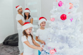 Vánoční rodinná tradice. Pár dětí Dívka a chlapec v Santa Klaus klobouk zdobení vánoční strom. Veselé Vánoce a šťastný nový rok