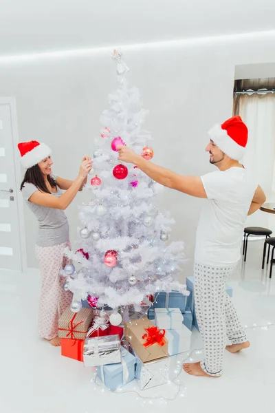 Família, x-mas, férias de inverno e conceito de pessoas - casal feliz decorando árvore de Natal em casa sobre luzes — Fotografia de Stock