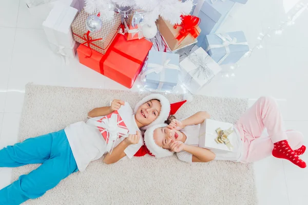 Напередодні Різдва. Хлопчик і дівчинка молодшого шкільного віку лежать на підлозі біля прикрашеної ялинки — стокове фото