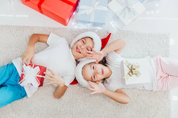 穿着睡衣的兄妹躺在圣诞树旁的地板上，还带着礼物 — 图库照片