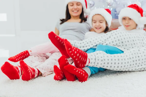 Famiglia felice in cappelli di Babbo Natale e calzini rossi seduti sul divano vicino all'albero di Natale con regali, isolati su bianco. focus selettivo — Foto Stock