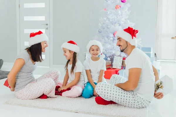 Familia en sombreros de Santa Claus intercambiando regalos frente al árbol de Navidad — Foto de Stock