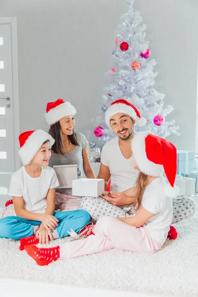 Feliz familia en Nochebuena. madre, padre e hijos descubren un regalo mágico en el árbol — Foto de Stock