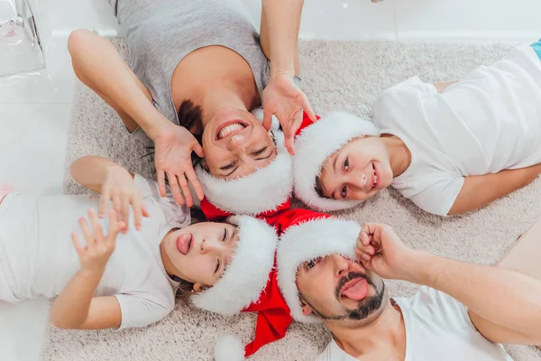 Щаслива сім'я з двома дітьми лежить під ялинкою з подарунками на килимі. Вид зверху — стокове фото