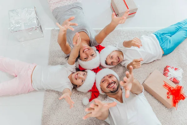 Ευτυχισμένη οικογένεια βρίσκονται στο χαλί κοντά σε όμορφα δώρα Χριστουγέννων. Απολαμβάνω να είμαστε μαζί την παραμονή της Πρωτοχρονιάς. πάνω όψη — Φωτογραφία Αρχείου