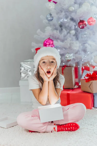 Fille heureuse ouvre un cadeau de Noël lumineux magique tout en étant assis près de l'arbre de Noël — Photo