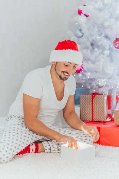Έκπληκτος νεαρός άνδρας ανοίξει ένα χριστουγεννιάτικο δώρο. Χριστουγεννιάτικη διάθεση. Νέο έτος — Φωτογραφία Αρχείου