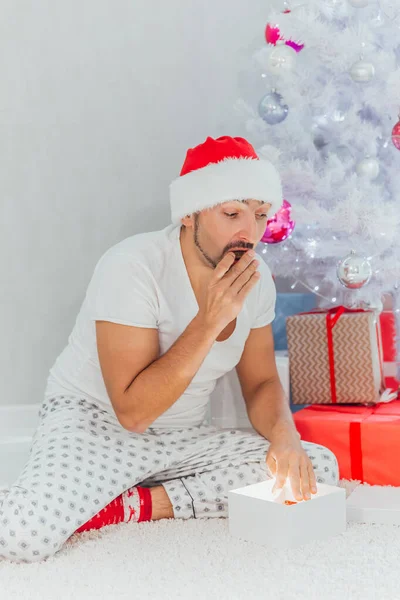 Έκπληκτος νεαρός άνδρας ανοίξει ένα χριστουγεννιάτικο δώρο. Χριστουγεννιάτικη διάθεση. Νέο έτος — Φωτογραφία Αρχείου