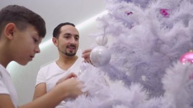 Bir Noel ağacını renkli bayraklarla süsleyen aile videosu oturma odasında..