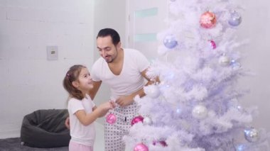 Küçük kızı ağacın üst dalına pembe bir mücevher asmak istiyor, bu yüzden babası onu seçiyor ve çok mutlu bir şekilde sarılıyorlar..
