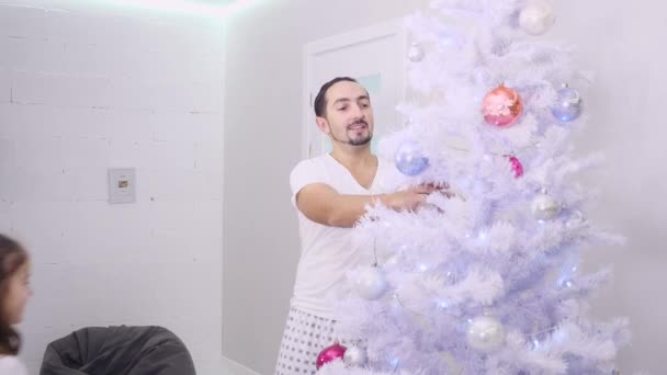 幸せな父親と隠された小さな娘が一緒にクリスマス・イブにモミの木を飾る. — ストック動画