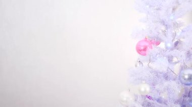 Beyaz gümüş ve pembe tonlarla süslenmiş Noel ağacı beyaz arka planda çelenklerle parıldıyor.